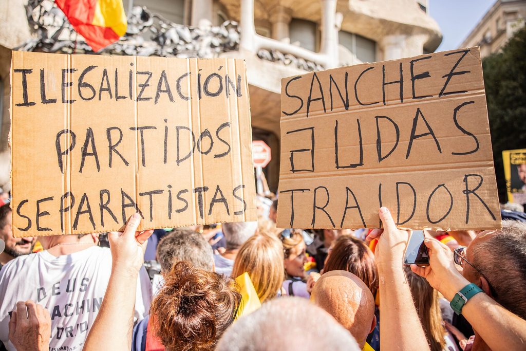 Signs of protesters criticising Sánchez and the Catalan independence movement at an SCC demonstration in Barcelona, 8 October 2023 (Photo: VOX Espana / Wikimedia Commons)