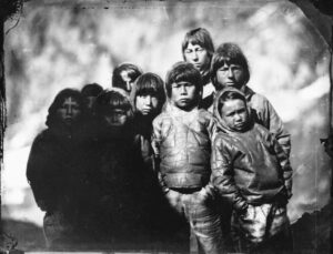 Nine Inuit children (probably all boys), wearing summer clothing made from seal skin. The children on the left are hidden in shadow. The negative has evidence of masking paper having been pasted onto the emulsion side. It is not known where this group was photographed. The Phoenix visited four settlements along the west coast of Greenland: Holsteinborg, Godhavn, Proven, and Upernarvick between 8 June and 21 July 1854. Photo: National Maritime Museum, Greenwich, London / Captain Edward Augustus Inglefield / Wikimedia Commons.