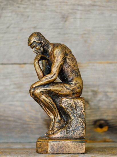 A bronze statue of a man in a pensive pose against a wooden background. Photo source: Quilia / Unsplash.